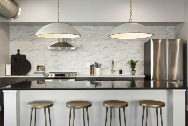 Modern kitchen with marble backsplash, large pendant lights, stainless steel fridge, and four metal stools at island at The Espen Residences