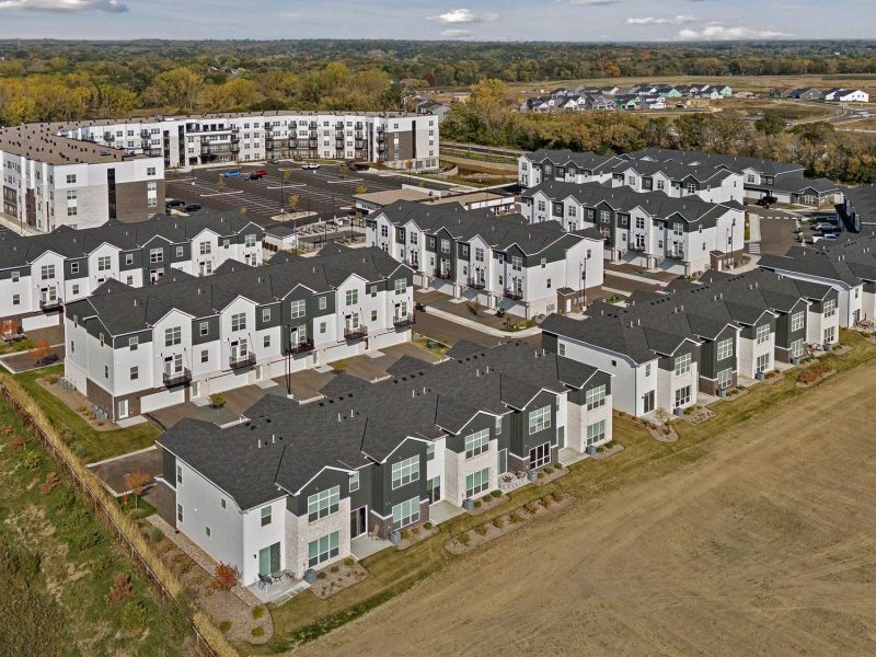 Aerial view of a modern townhouse and apartment complex surrounded by open fields and trees.
