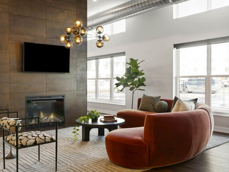 A modern lounge space at The Espen Residences in Oakdale, MN, featuring contemporary seating, a fireplace with mounted TV, large windows, and warm natural lighting.