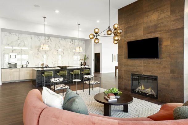 A stylish resident lounge at The Espen Residences in Oakdale, MN, featuring a fireplace with mounted TV, modern seating, a round coffee table, pendant lighting, and a kitchen-style bar area in the background.