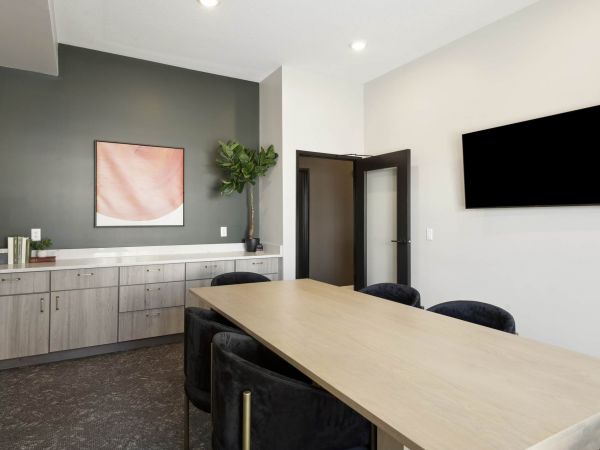 The conference room at The Espen Residences in Oakdale, MN, featuring a long meeting table, modern chairs, built-in cabinetry, and a wall-mounted TV in a clean, professional setting.