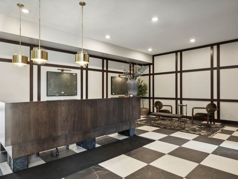 Modern hotel lobby with a checkered floor, wood reception desk, and a small seating area with chairs.