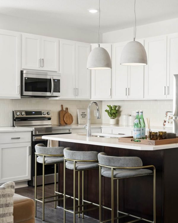 Modern kitchen with white cabinets, pendant lights, an island with stools, and stainless steel appliances.