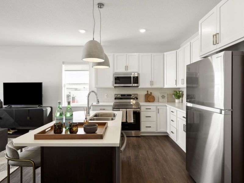 A modern kitchen at The Espen Residences in Oakdale, MN, featuring white cabinetry, stainless steel appliances, a center island with seating, pendant lighting, and wood-style flooring.
