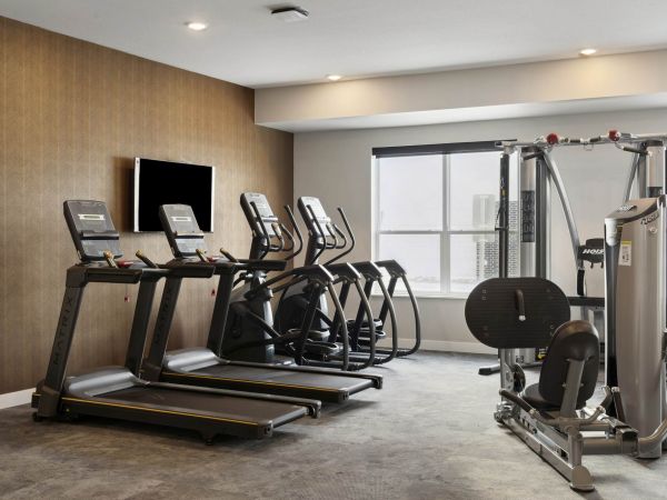 The fitness center at The Espen Residences in Oakdale, MN, featuring treadmills, ellipticals, strength equipment, and a large window that brings in natural light.