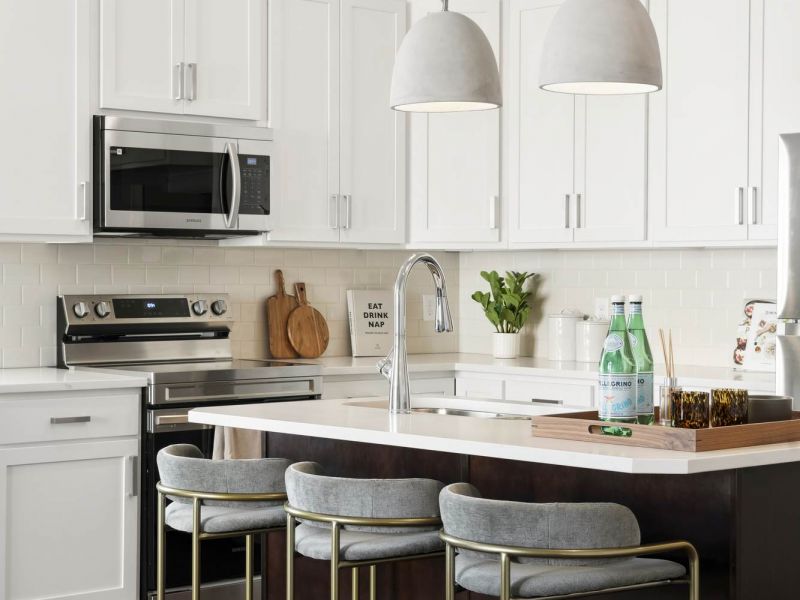 Modern kitchen with white cabinets, pendant lights, an island with stools, and stainless steel appliances.