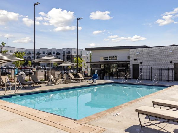 The outdoor pool area at The Espen Residences in Oakdale, MN, featuring lounge seating, clear blue water, and a modern clubhouse under a sunny sky.